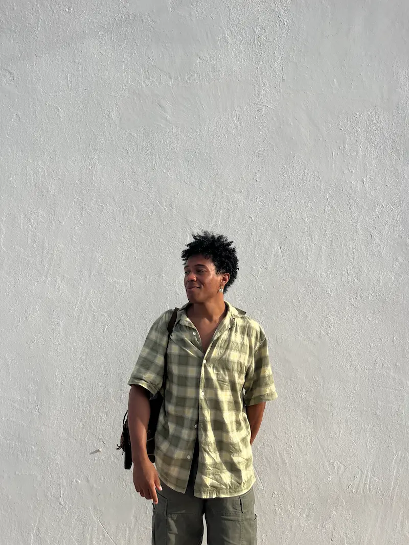 Mann in kariertem Hemd und grauer Hose steht vor einer weißen Wand