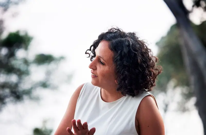  Dunkelhaarige Frau mit schulterlangen Locken und weißem ärmellosem Oberteil