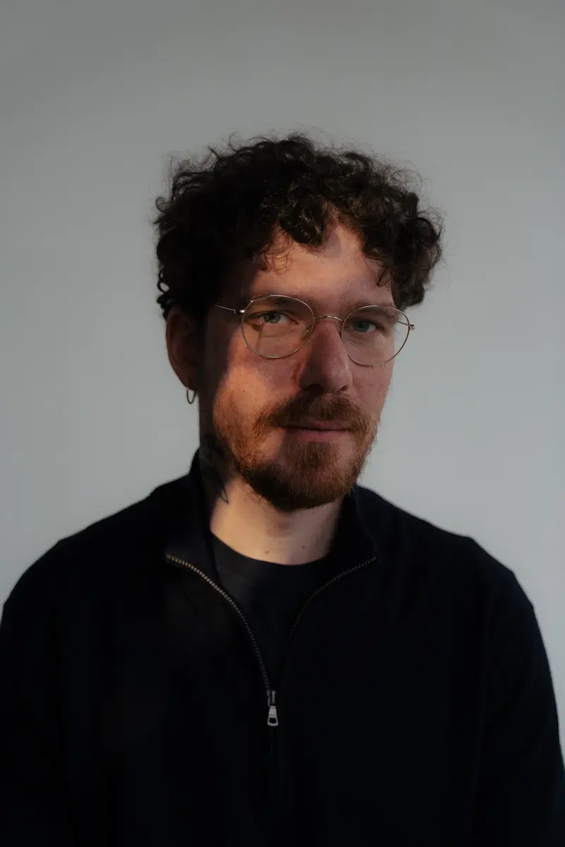 Mann mit lockigen Haaren, Brille und schwarzem Oberteil