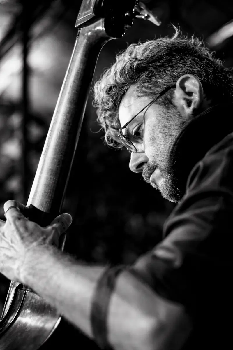 Schwarzweiß Porträtfoto von Mimis Sandalis. Er spielt Kontrabass und blickt konzentriert auf sein Instrument