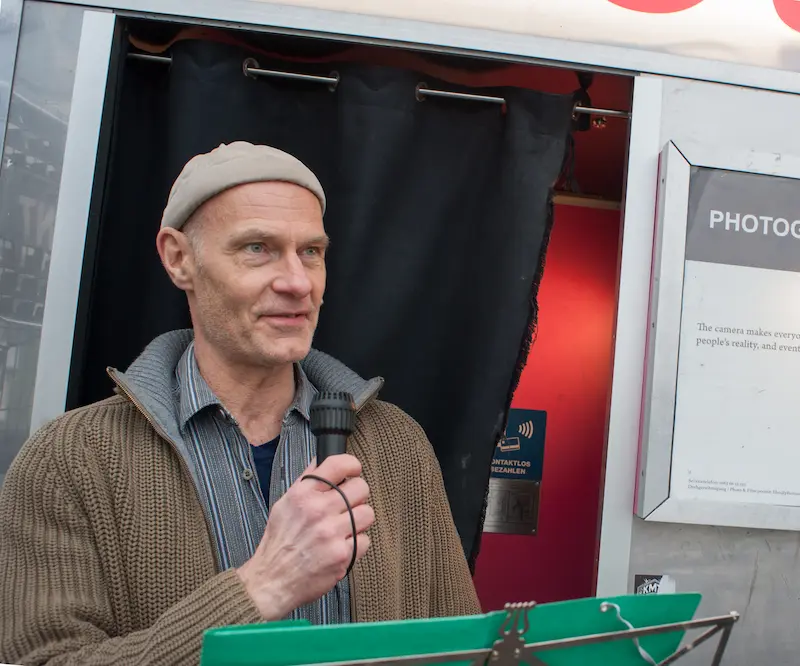 Michael Janßen trägt eine graue Mütze und hält ein Mikrophon in der Hand