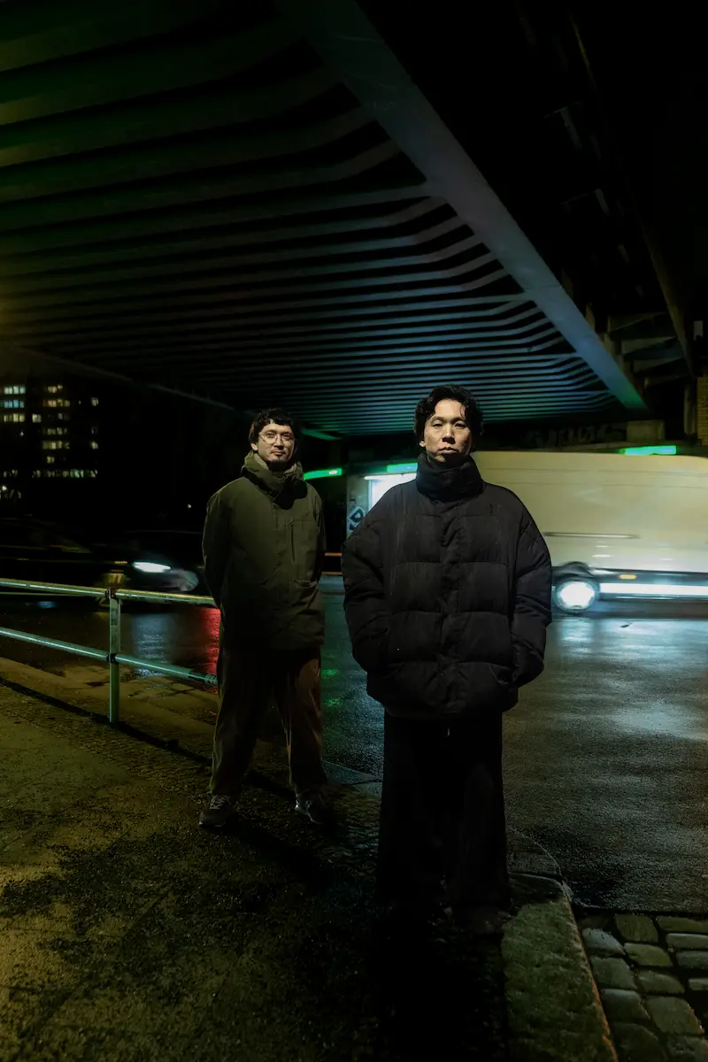 Das Duo steht in einer Unterführung, es ist Nacht. Dunkel gekleidet blicken sie leicht versetzt stehend in die Kamera.
