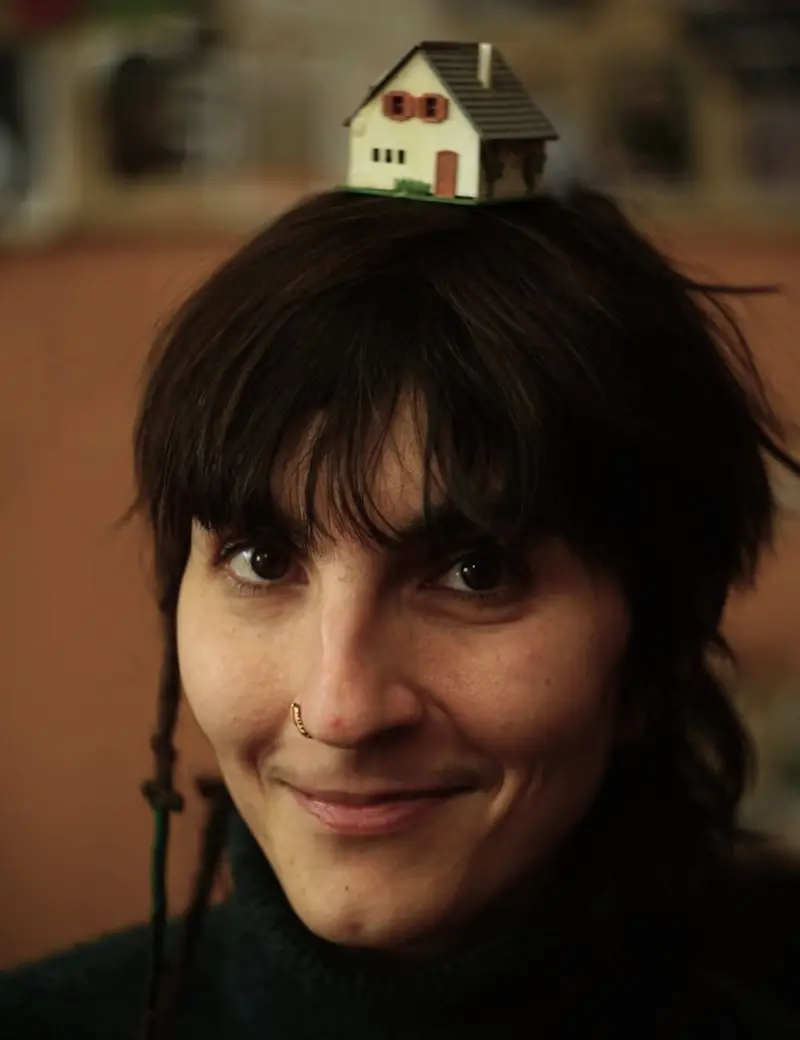 Ein Porträt von Alice Muitoevoli Rugai. Alice Muitoevoli Rugai hat dunkle Haare, einen Pony, ein Nasenpiercing, auf dem Kopf ein kleines Spielzeughaus.