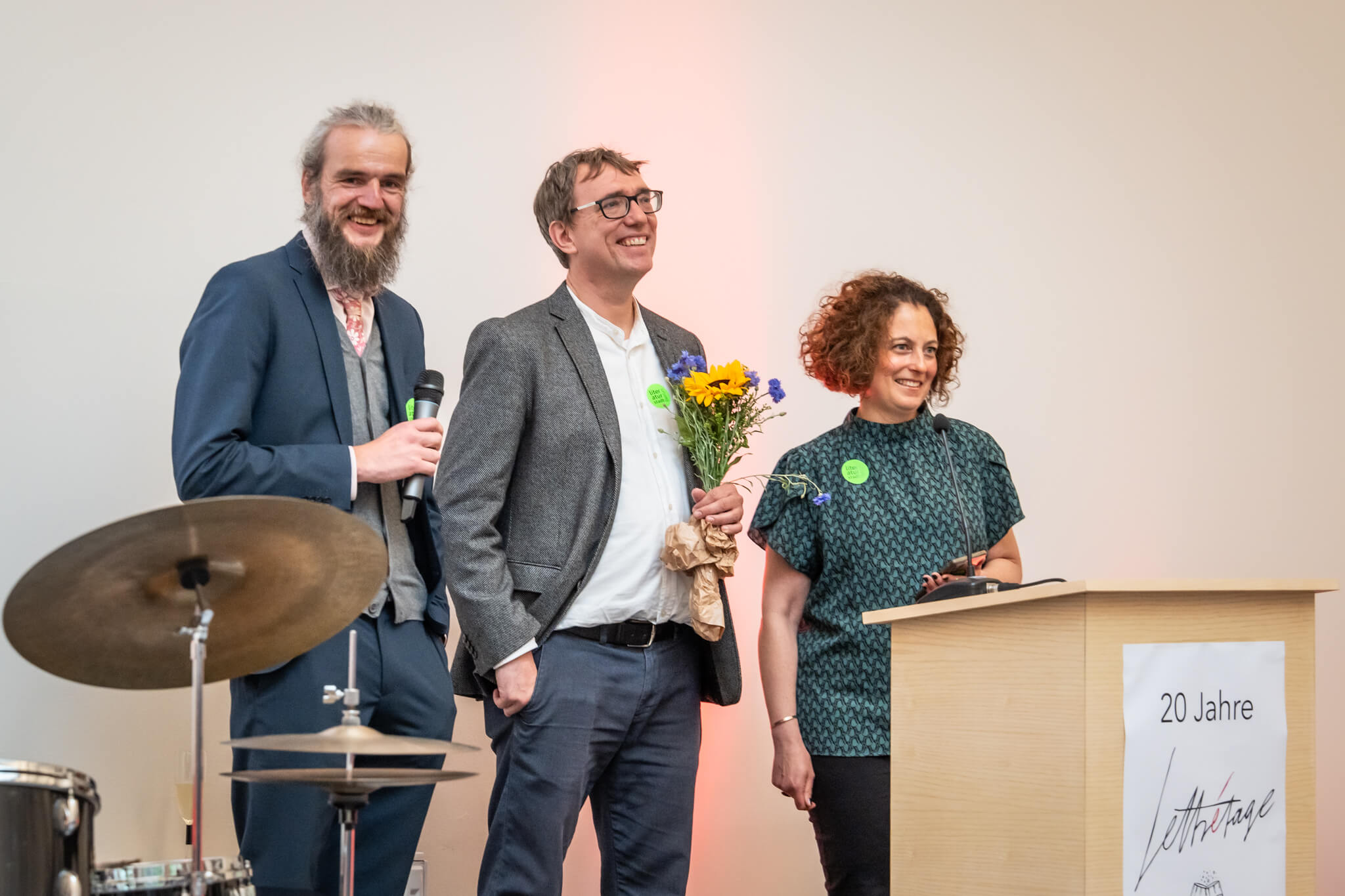 Die drei Lettrétage-Gründerinnen Tom, Moritz und Katharina stehen auf der Bühne und lächeln