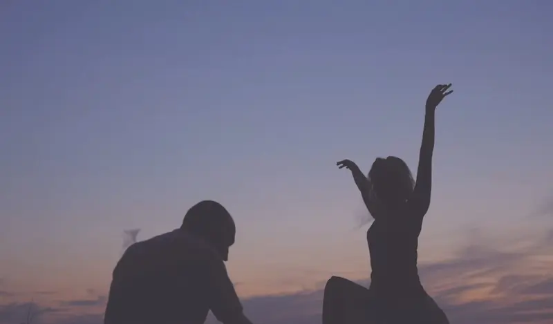 two human silhouettes in front of a pink-blue sky
