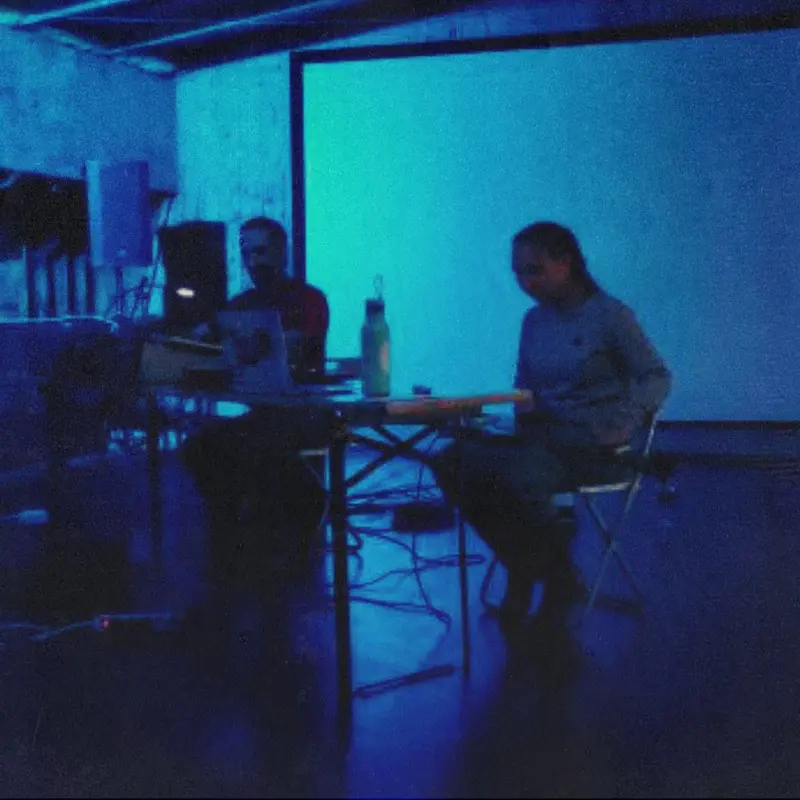 two people sitting in a desk, blue-lit room