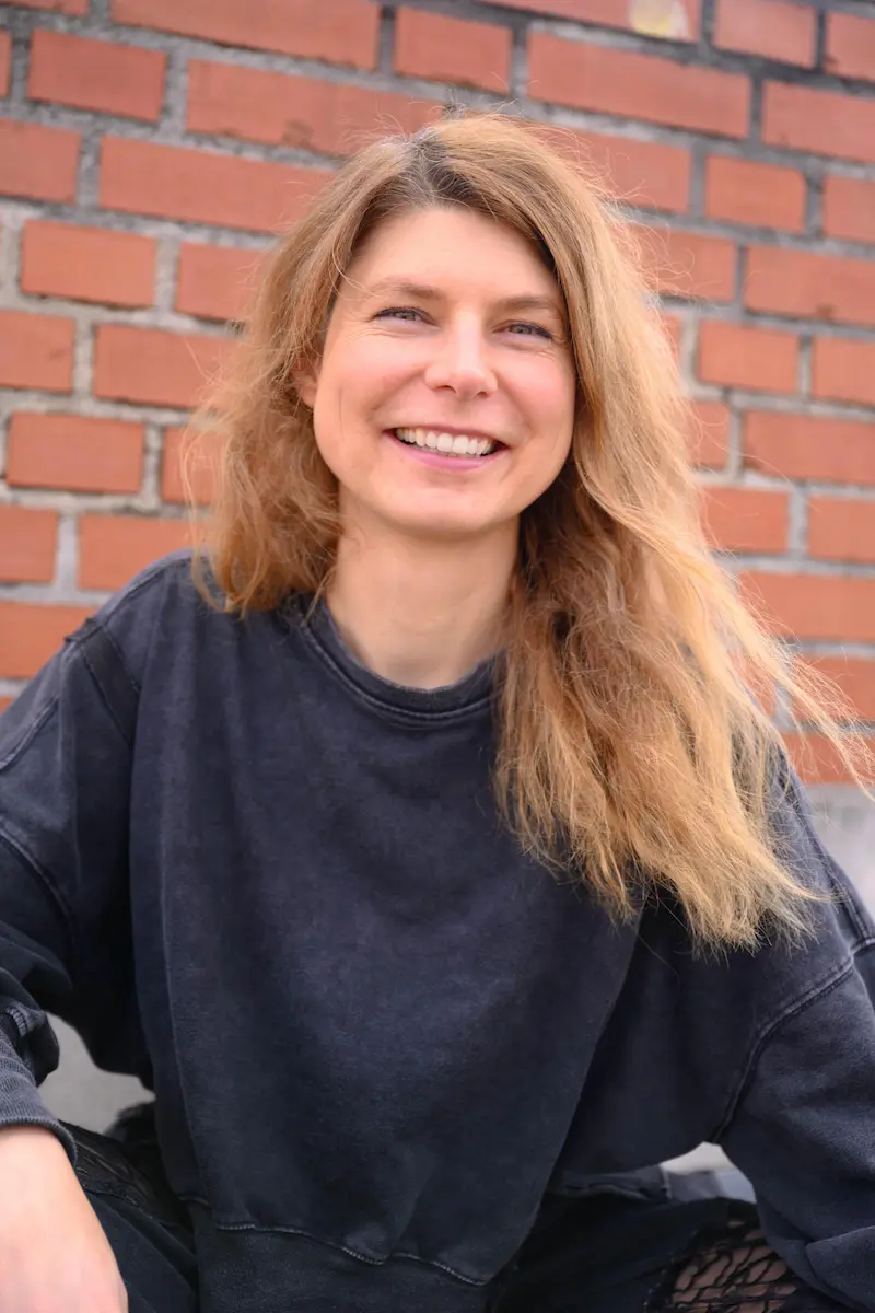 portrait of the artist wearing black sweater, brick wall in the background