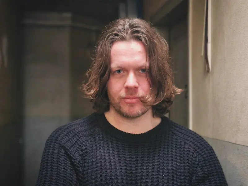 portrait of the artist standing in hallway wearing black sweater