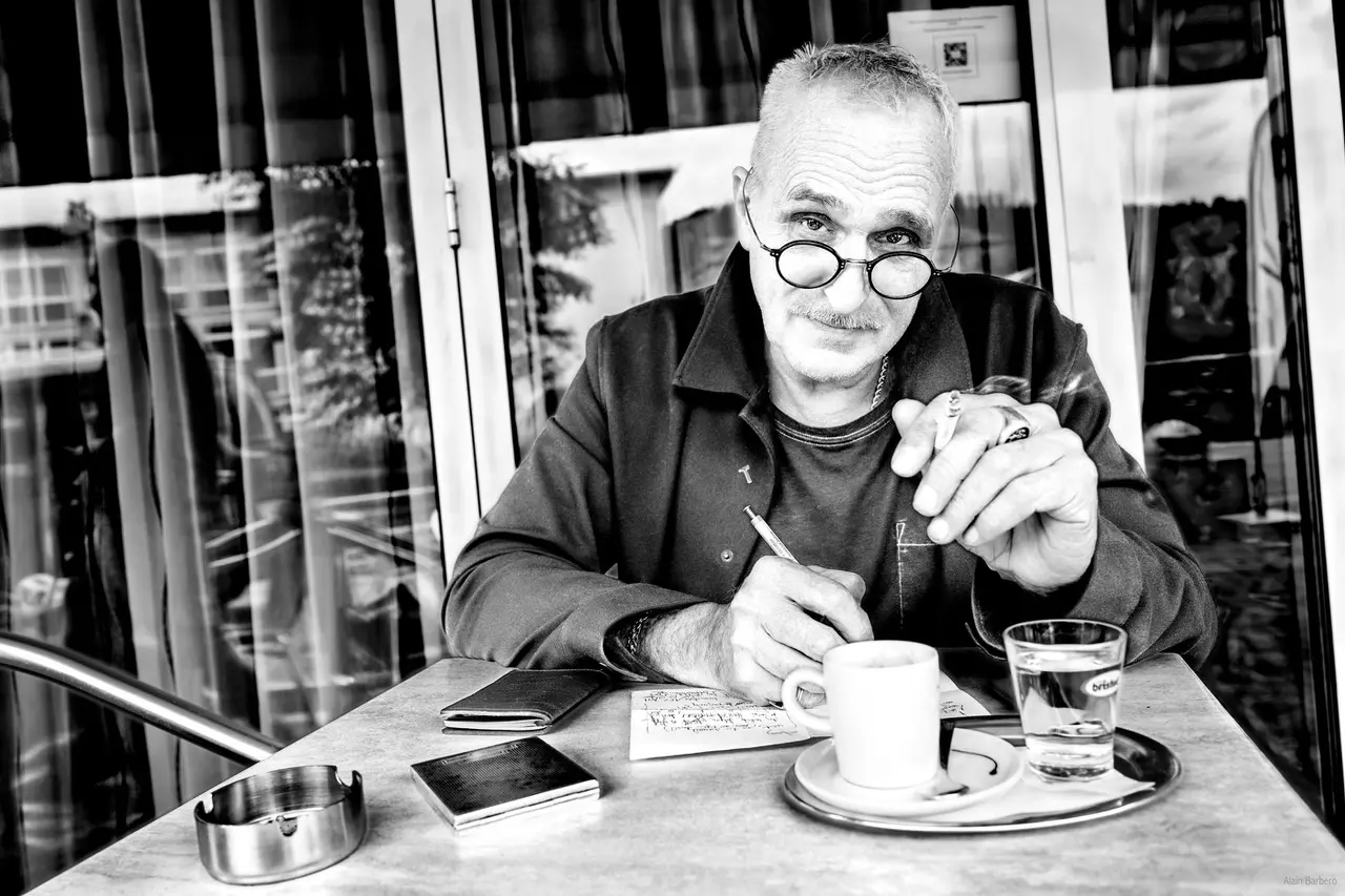Alain Barbero sitzt an einem Cafétisch und schreibt.