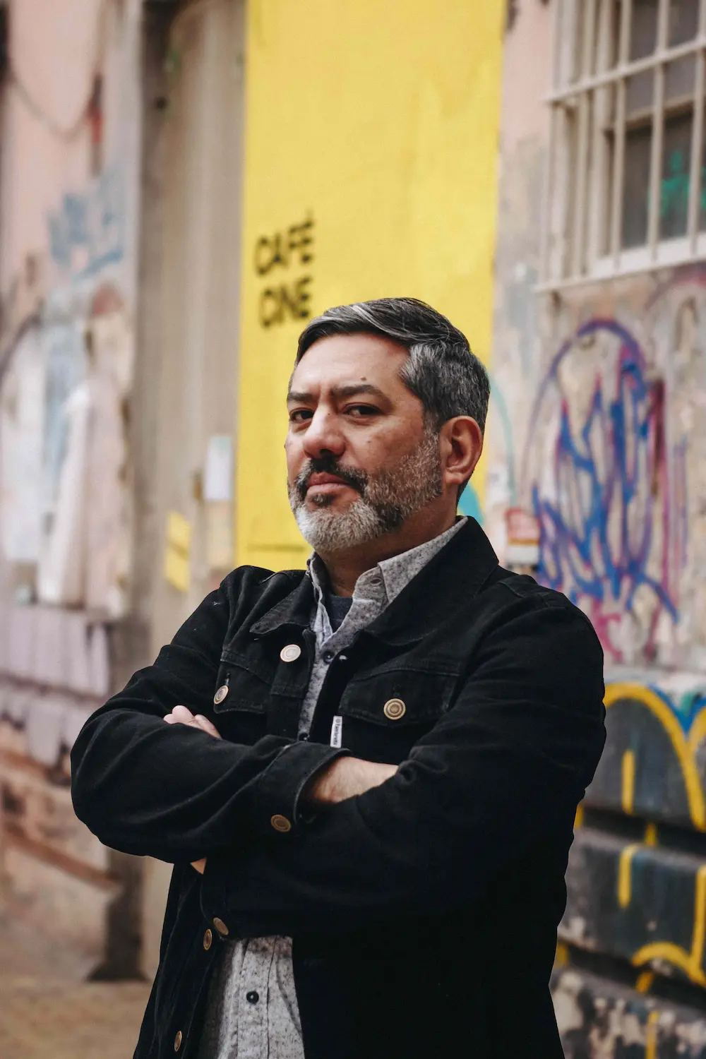 Carlos Soto Roman steht mit verschränkten Armen vor einer mit GRaffiti besprühten Hauswand.