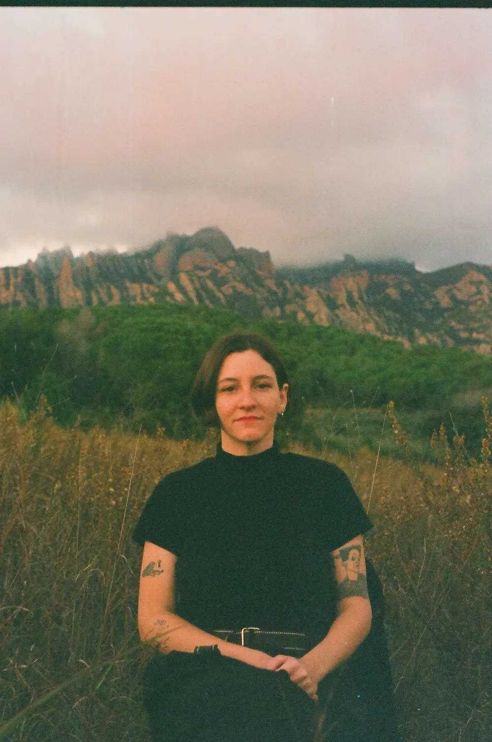 Karen Byk sitzt in einem Feld, im Hintergrund sieht man Berge.