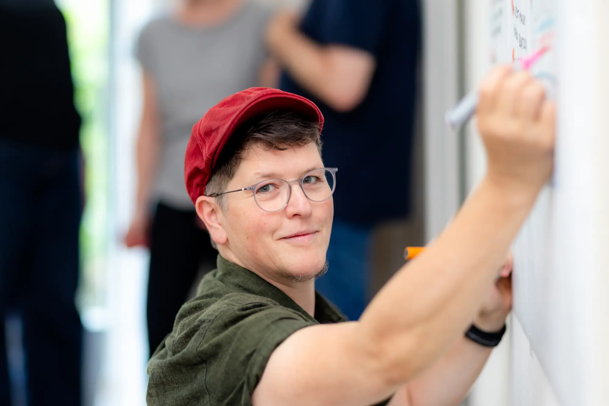 Jona Neugebauer malt mit Markern an ein Whiteboard und lächelt dabei in die Kamera
