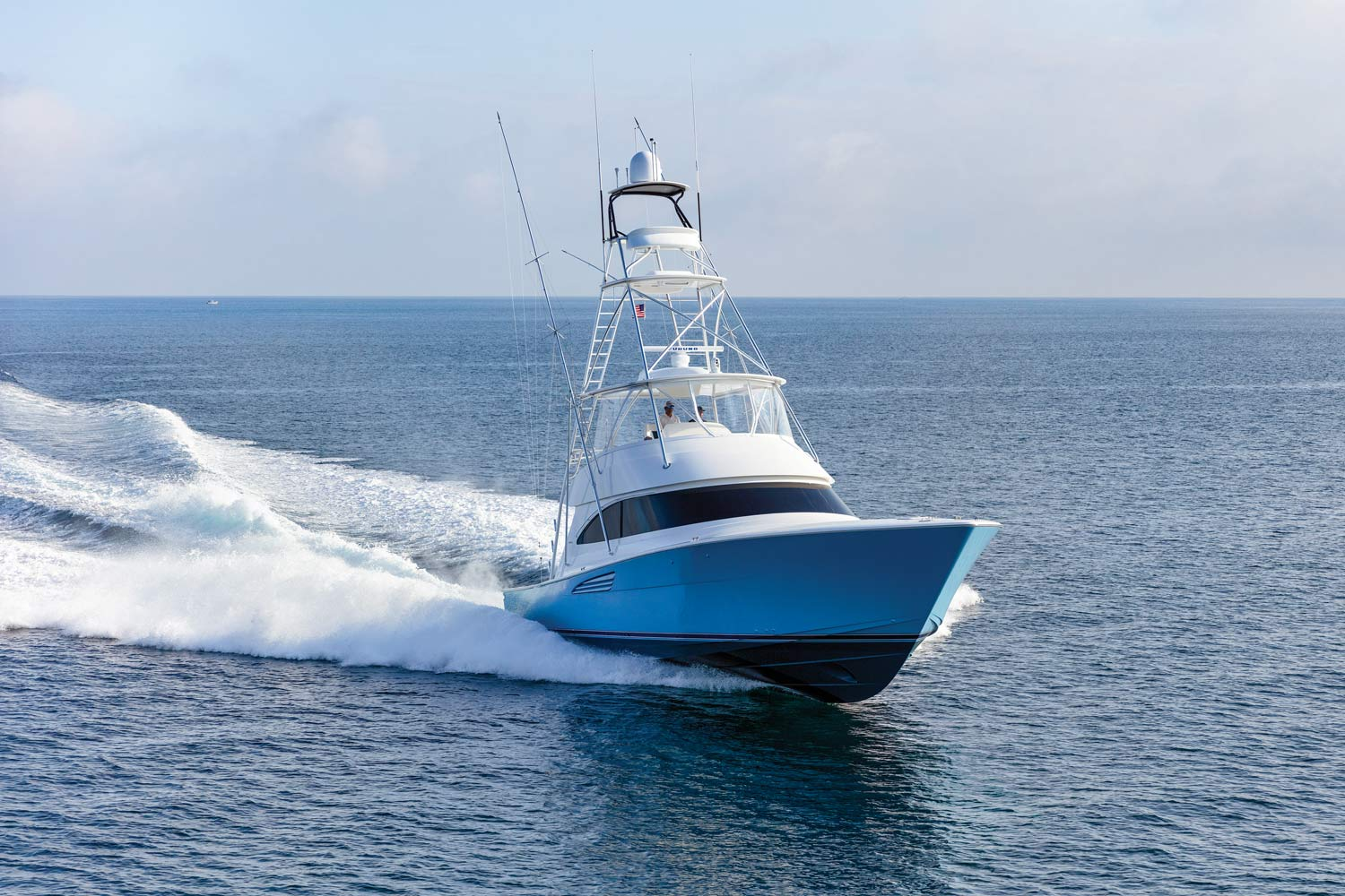 Blue and white sport fishing yacht speeding on calm ocean water creating a white wake.
