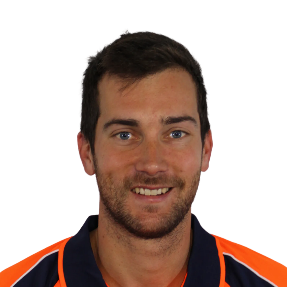Smiling man with short dark hair and blue eyes wearing an orange and navy collared shirt.