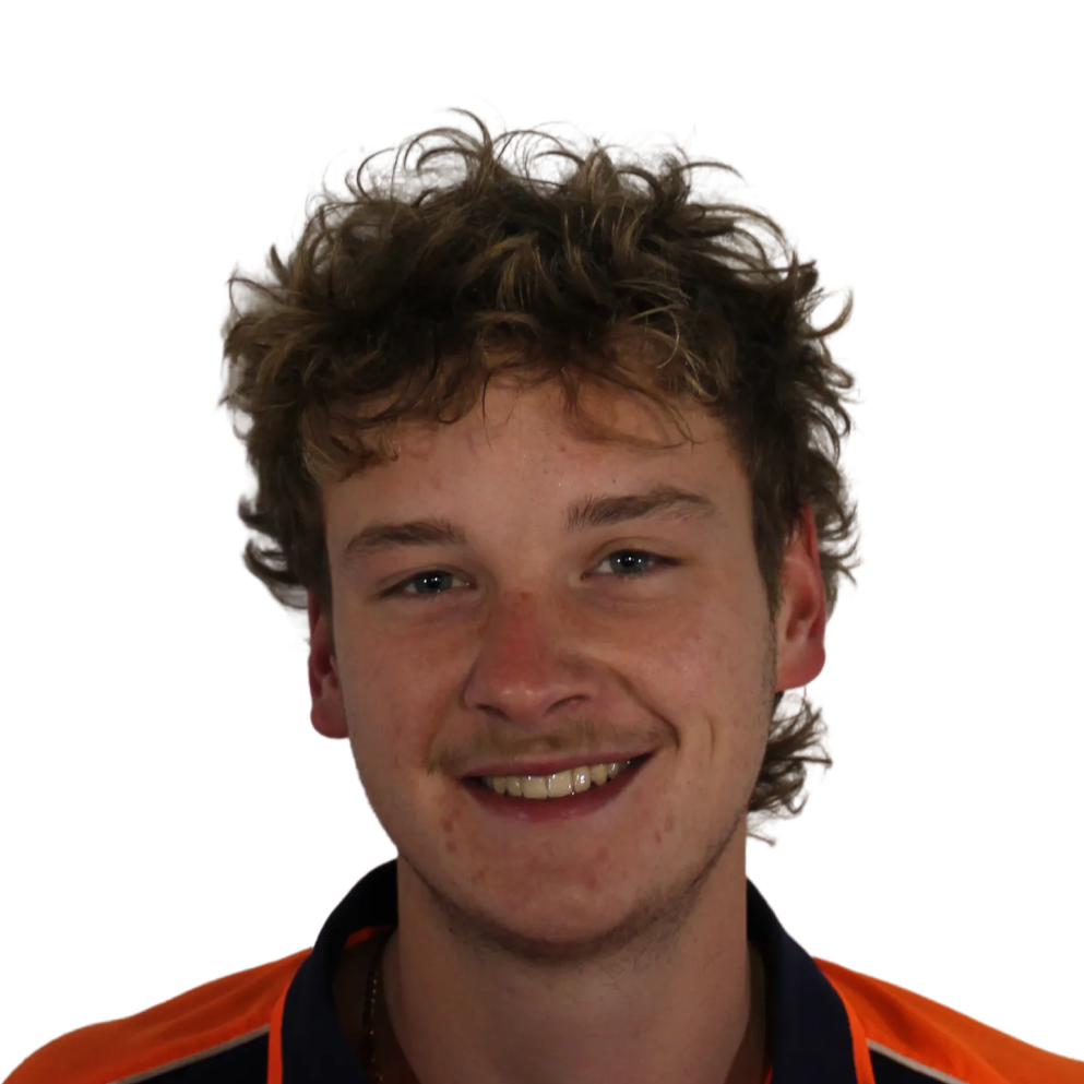 Young man with curly hair wearing an orange and navy shirt smiling at the camera.