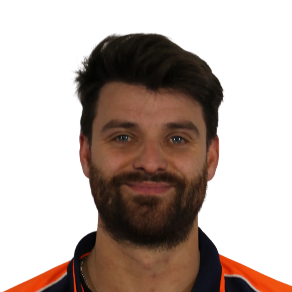 Smiling man with dark hair and beard wearing an orange and navy shirt.
