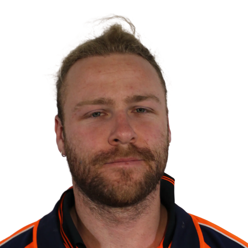 Close-up of a bearded man with light brown hair tied back, wearing a dark blue and orange jacket.