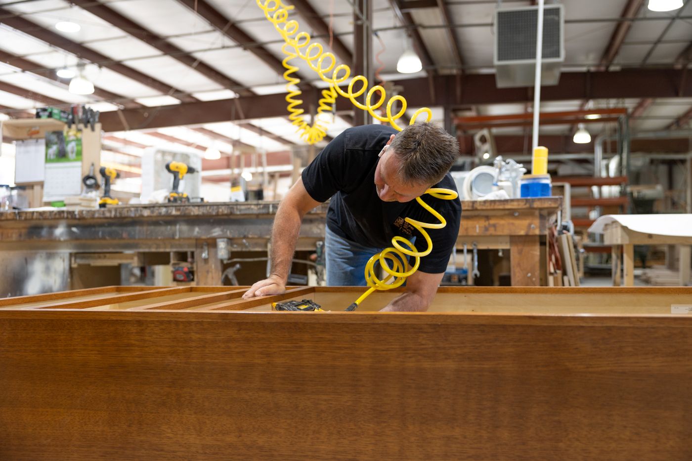 Man using an air-powered nail gun on a wooden cabinet frame in a woodworking shop.
