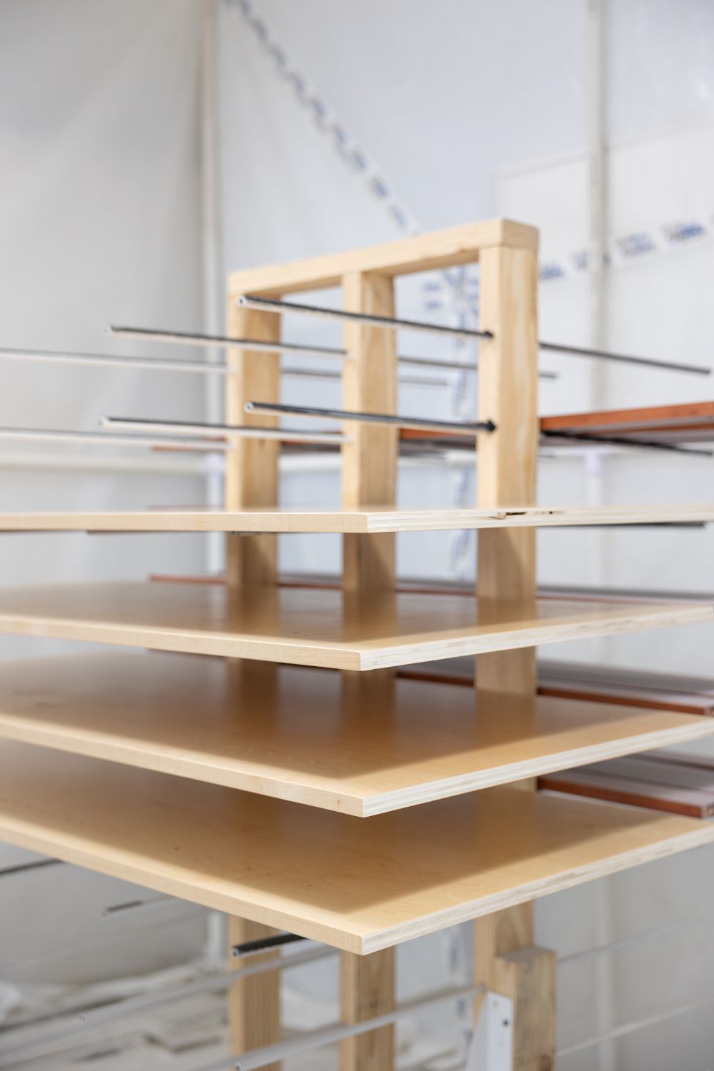 Stack of large, flat wooden boards separated by metal rods on a wooden frame in a workshop.