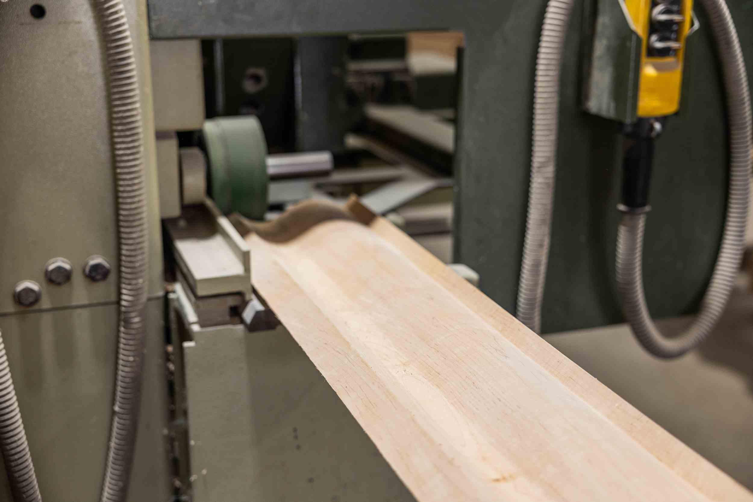 Wooden board with a decorative curved profile being shaped on a spindle molder machine.