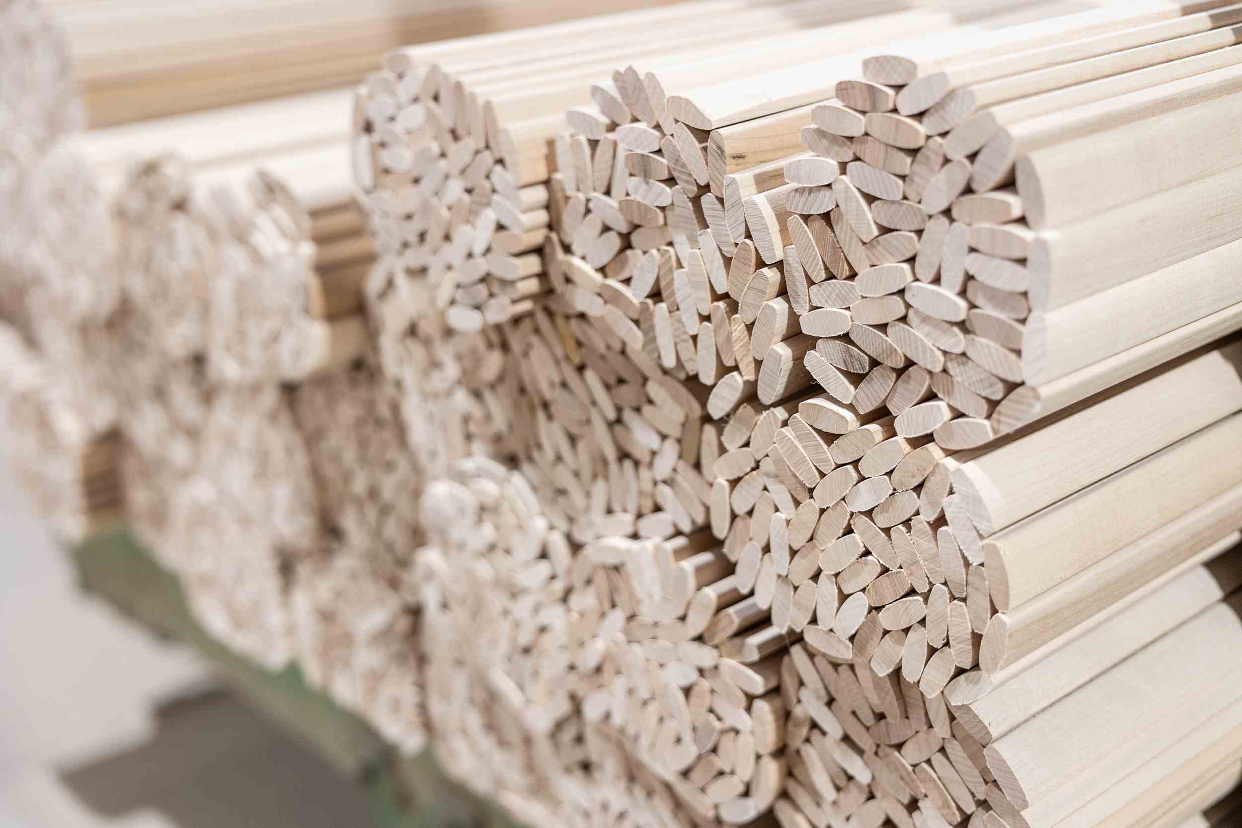 Close-up of bundled, light-colored wooden dowels stacked in a factory or workshop.