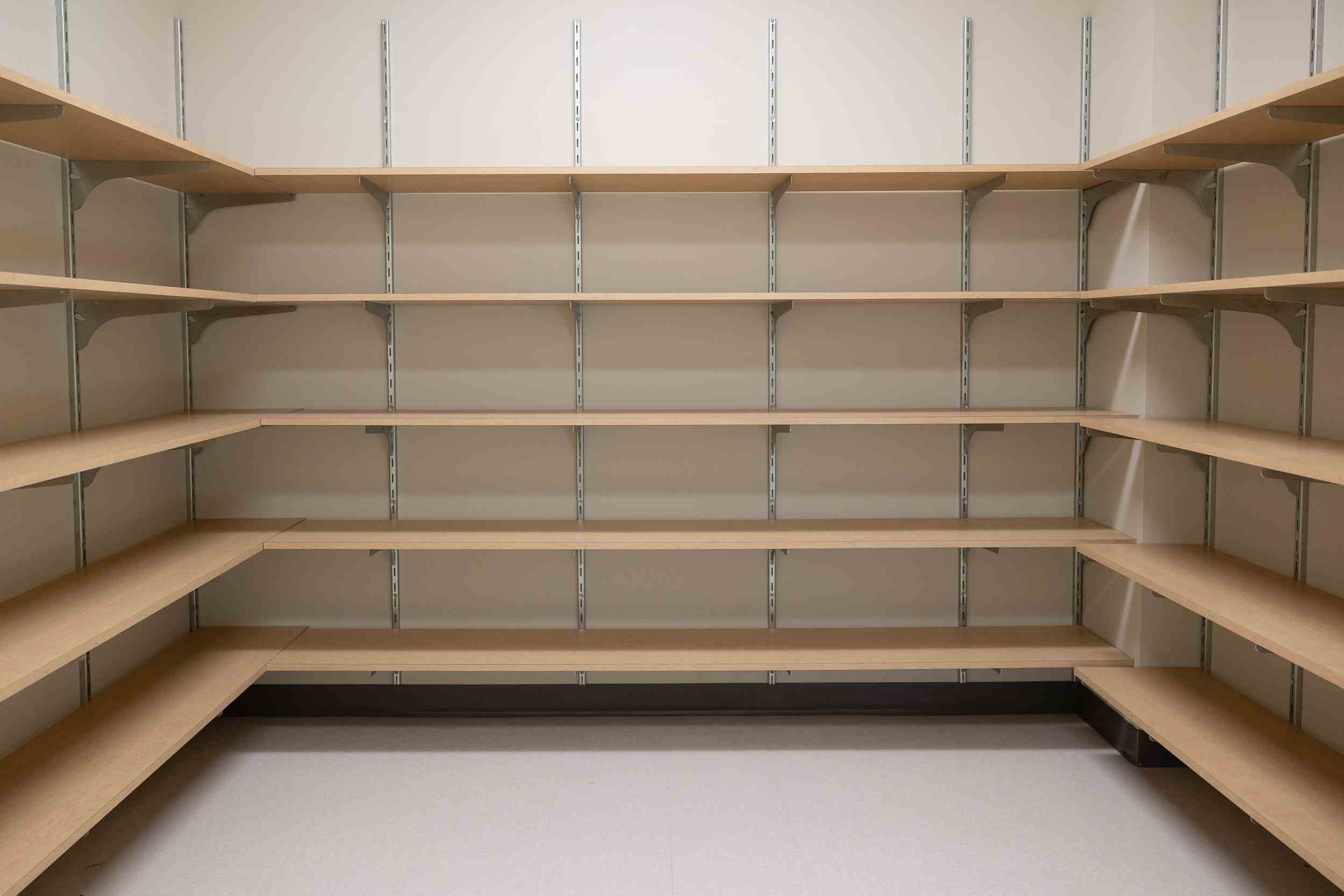 Empty corner shelving unit with multiple wooden shelves against beige walls and white floor.