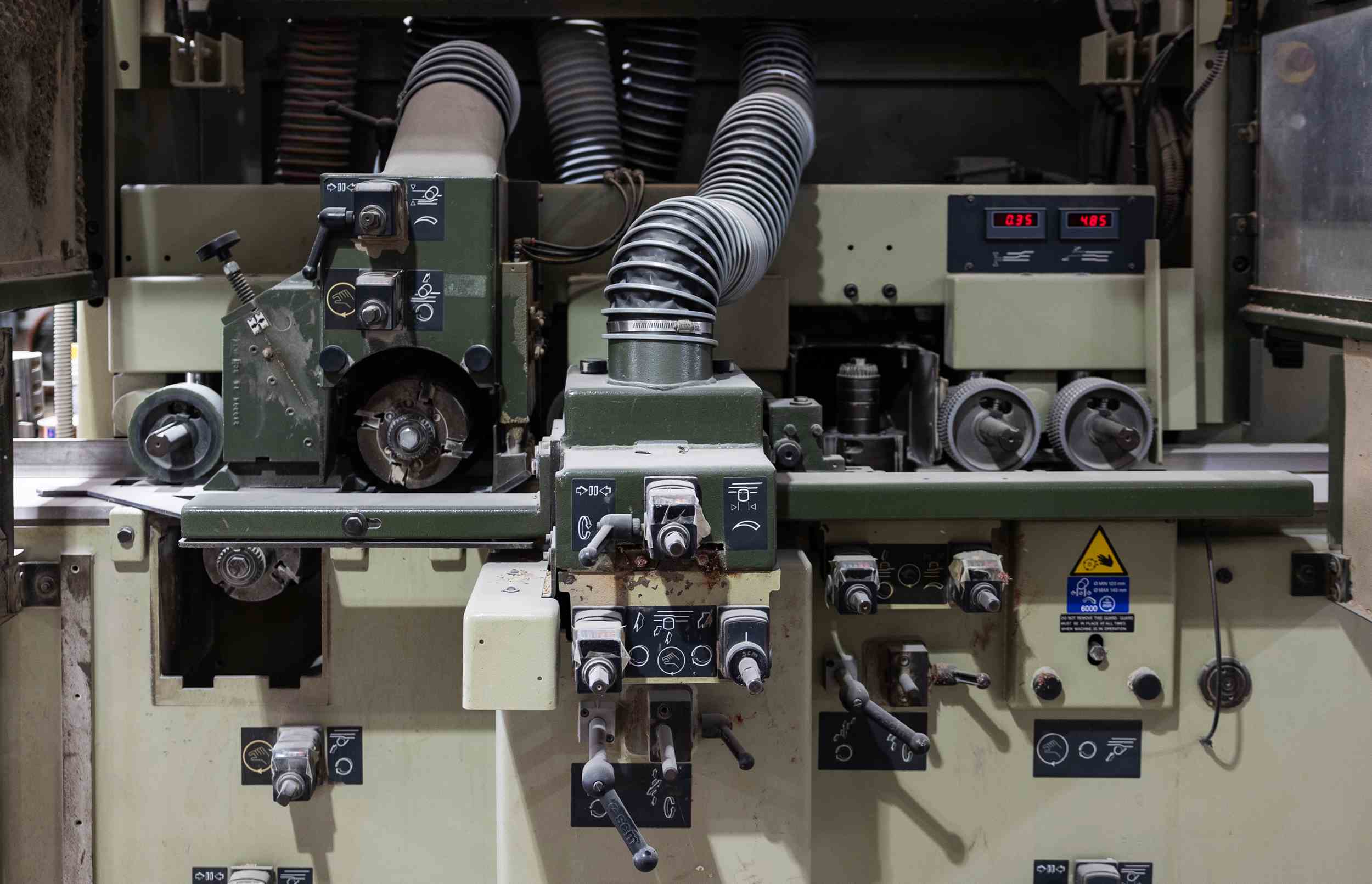 Close-up of industrial woodworking machine with various knobs, levers, tubes, and safety warning labels.