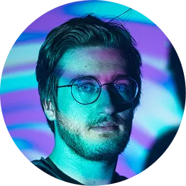 Portrait of a man with glasses and beard illuminated by blue and purple light patterns on his face and background.
