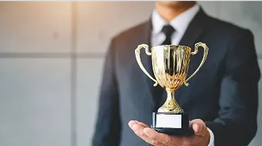 Person in a business suit holding a gold trophy with blank plaque.