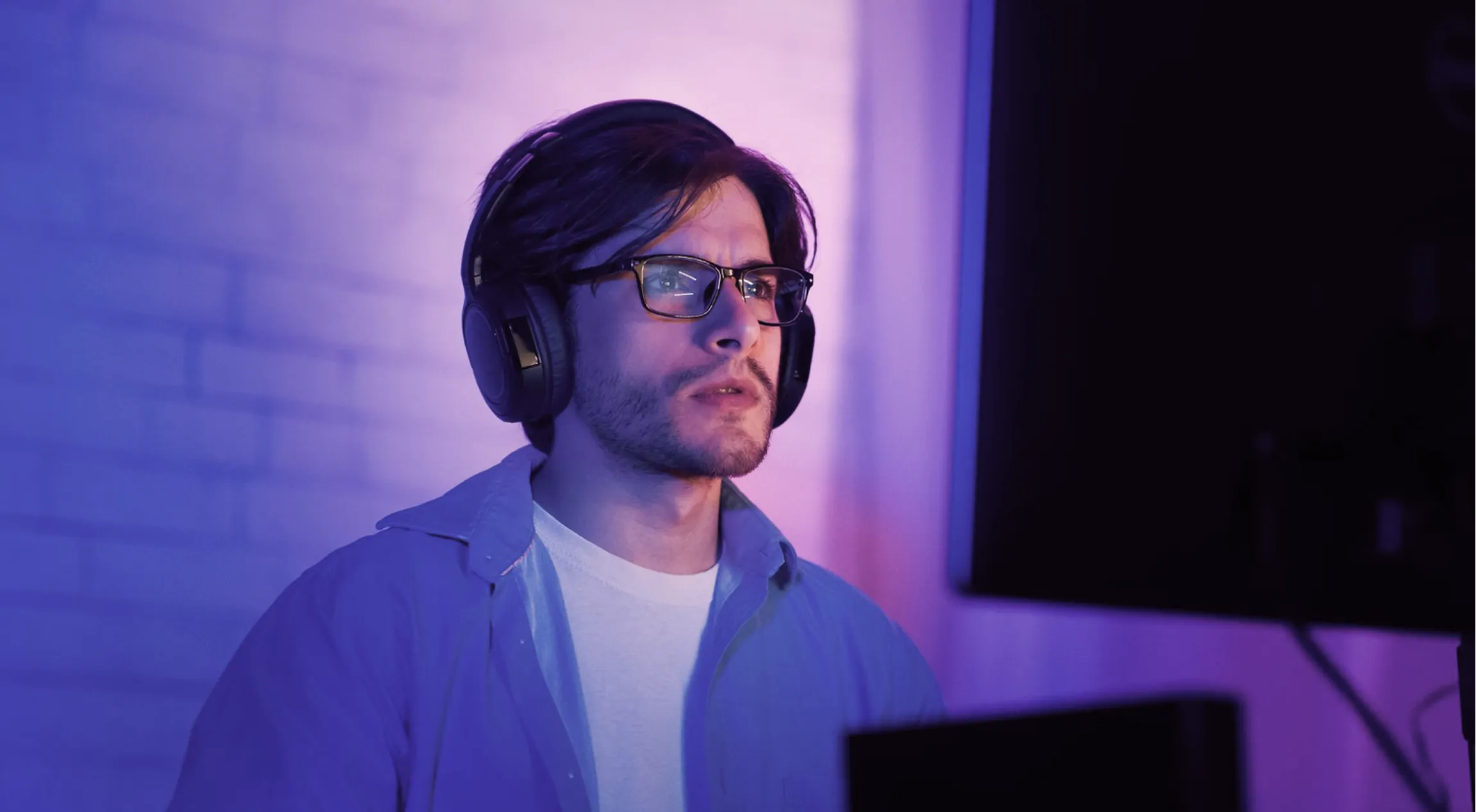 Young man smiling and wearing a virtual reality headset and headphones in a purple hoodie with colorful lighting.