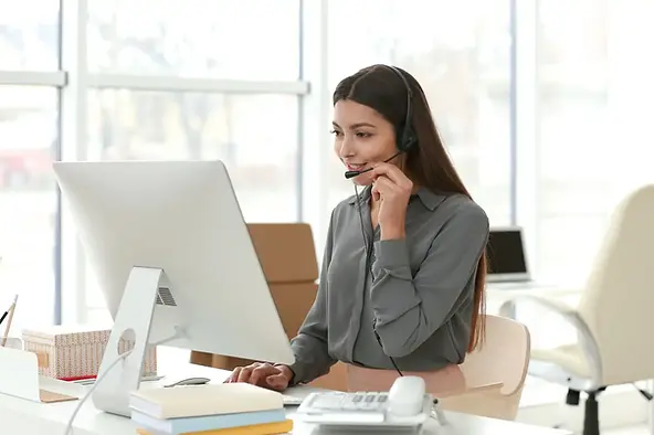 Managing remote team workflows during a video call in a bright office with a desktop and headset.