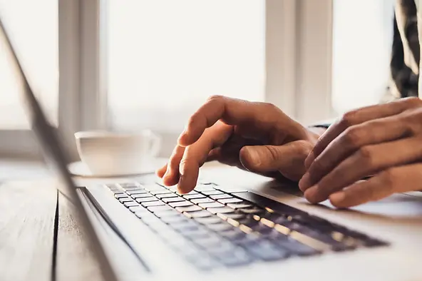 U.S.-based virtual assistant services shown through close-up of hands typing on a laptop beside a coffee cup.