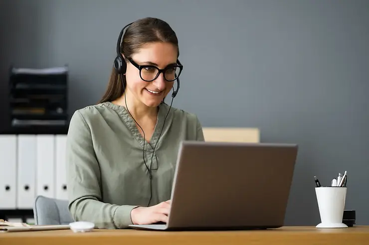 VA for business development smiling while working remotely on a laptop with a headset in a home office.