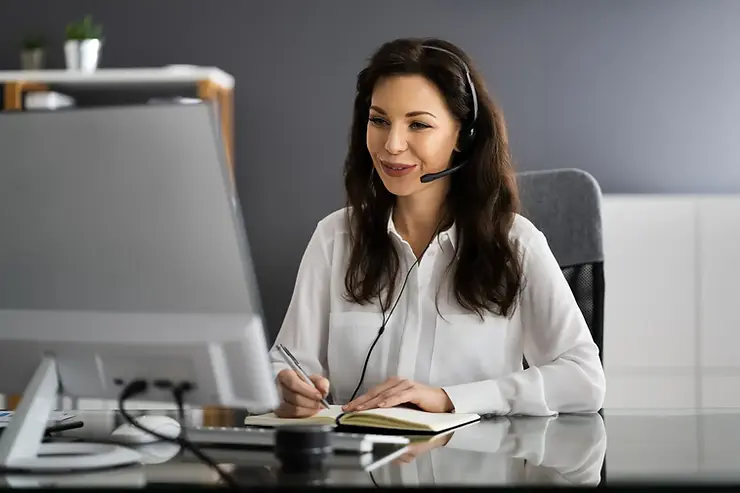 American virtual assistant offering professional support with a headset while writing in a notebook at a desk.