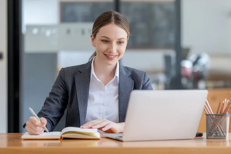 Remote virtual assistant taking notes while working on a laptop in a professional workspace.