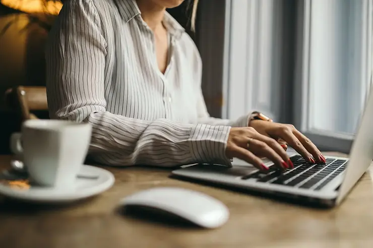 Remote business support professional typing on a laptop with coffee and notepad on a wooden desk.
