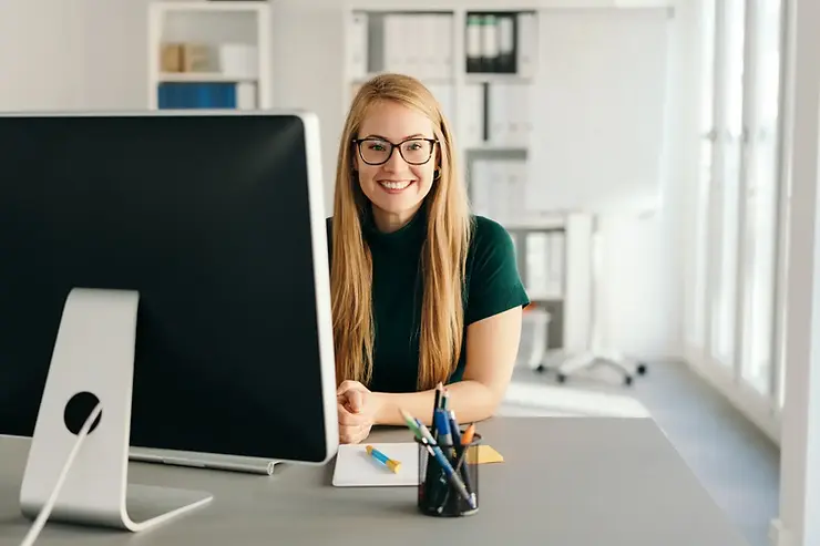 Virtual assistant services provided by a smiling woman using a desktop computer in a well-lit modern office.