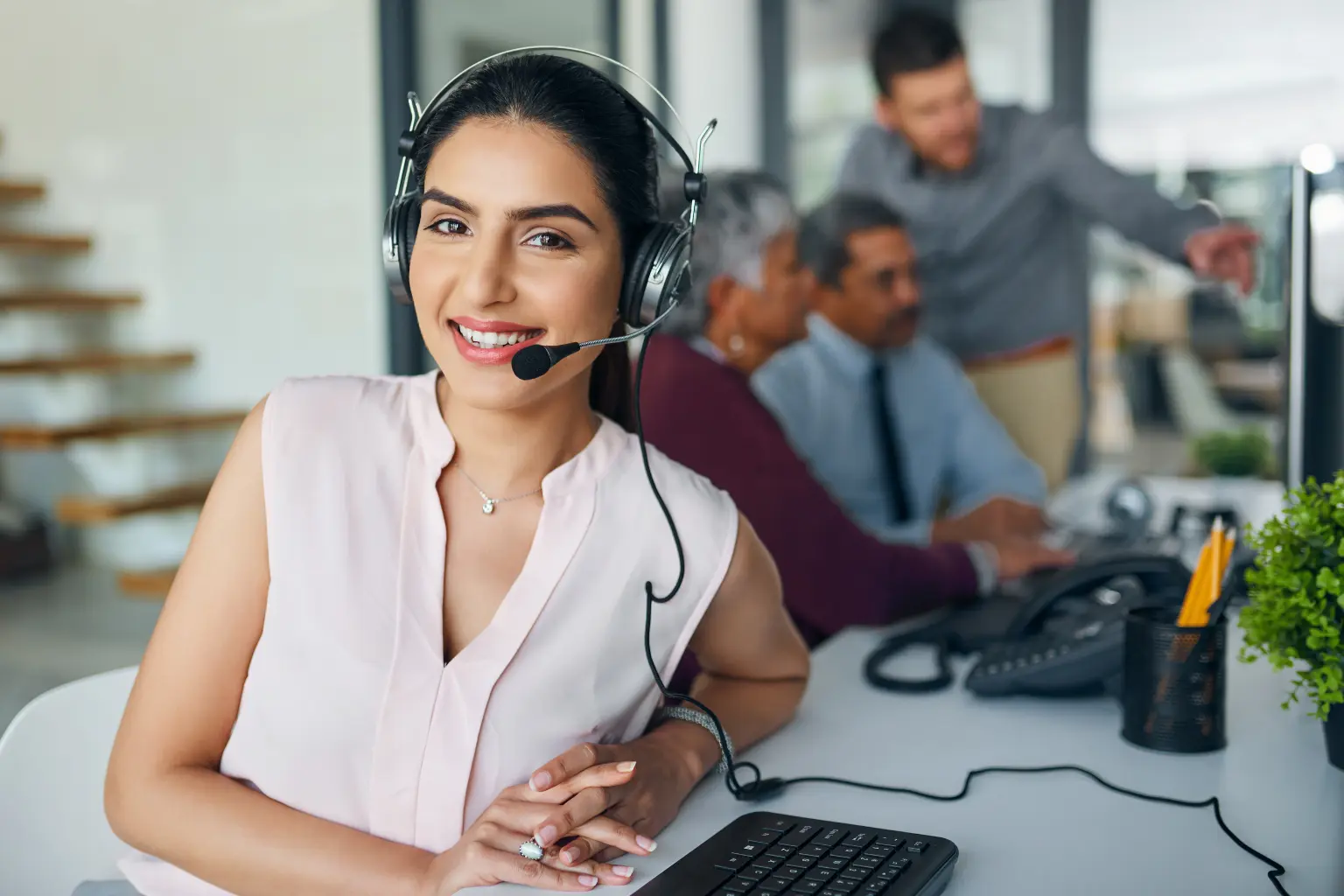 Remote executive assistant smiling while wearing a headset and working in a collaborative office environment.