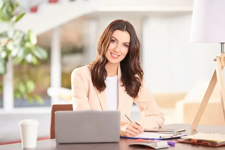 Virtual assistant USA professional writing notes while working on a laptop in a bright modern office.