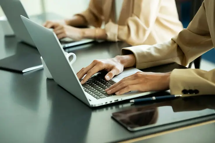 US-based virtual assistant typing on a laptop in a professional workspace with tablet and notebook nearby.