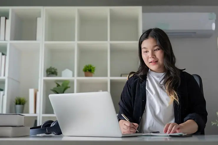 Remote executive assistants providing virtual support while writing in a notebook during a video meeting.
