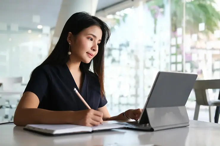 American virtual assistant services provider taking notes while using a tablet and stylus in a bright office.