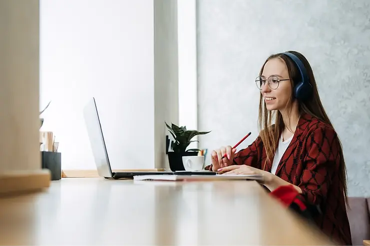 Virtual assistant staffing services agent wearing headphones and smiling while working remotely on a laptop.