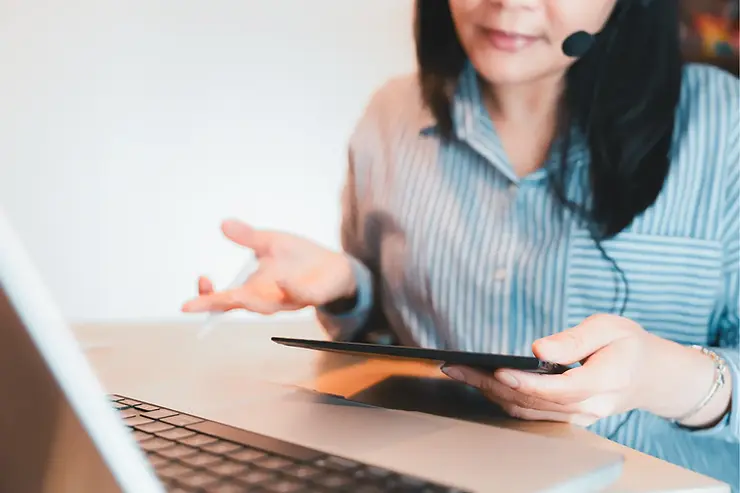 Virtual assistant wearing a headset gesturing expressively while holding a tablet during a remote client call.