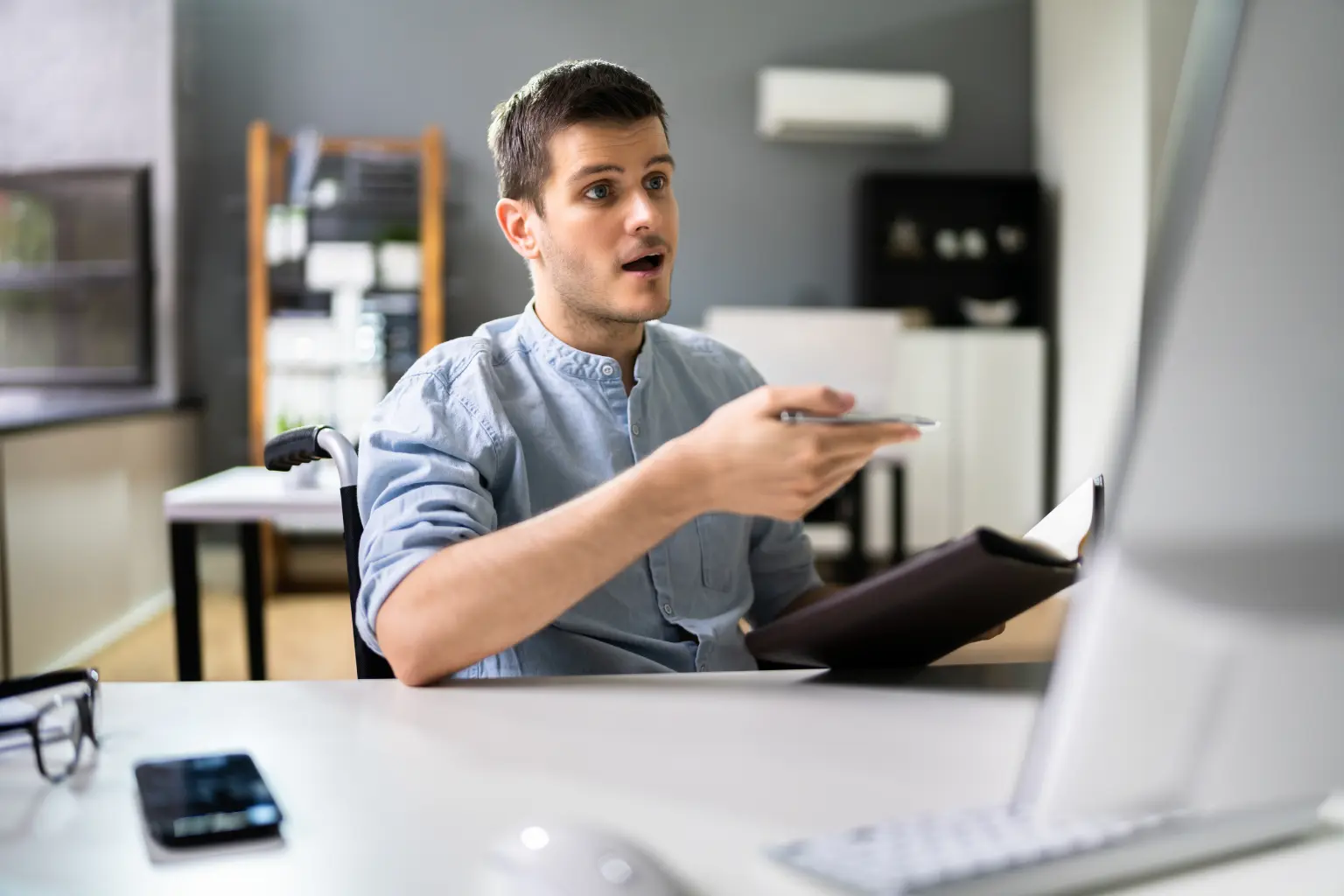 Virtual assistant gesturing expressively with a pen and notepad during a video call at an office desk.
