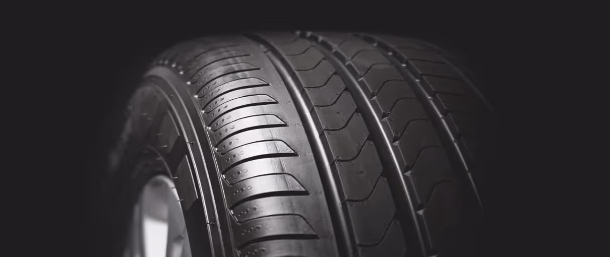 Close-up of a black car tire tread with detailed grooves and patterns on a dark background.
