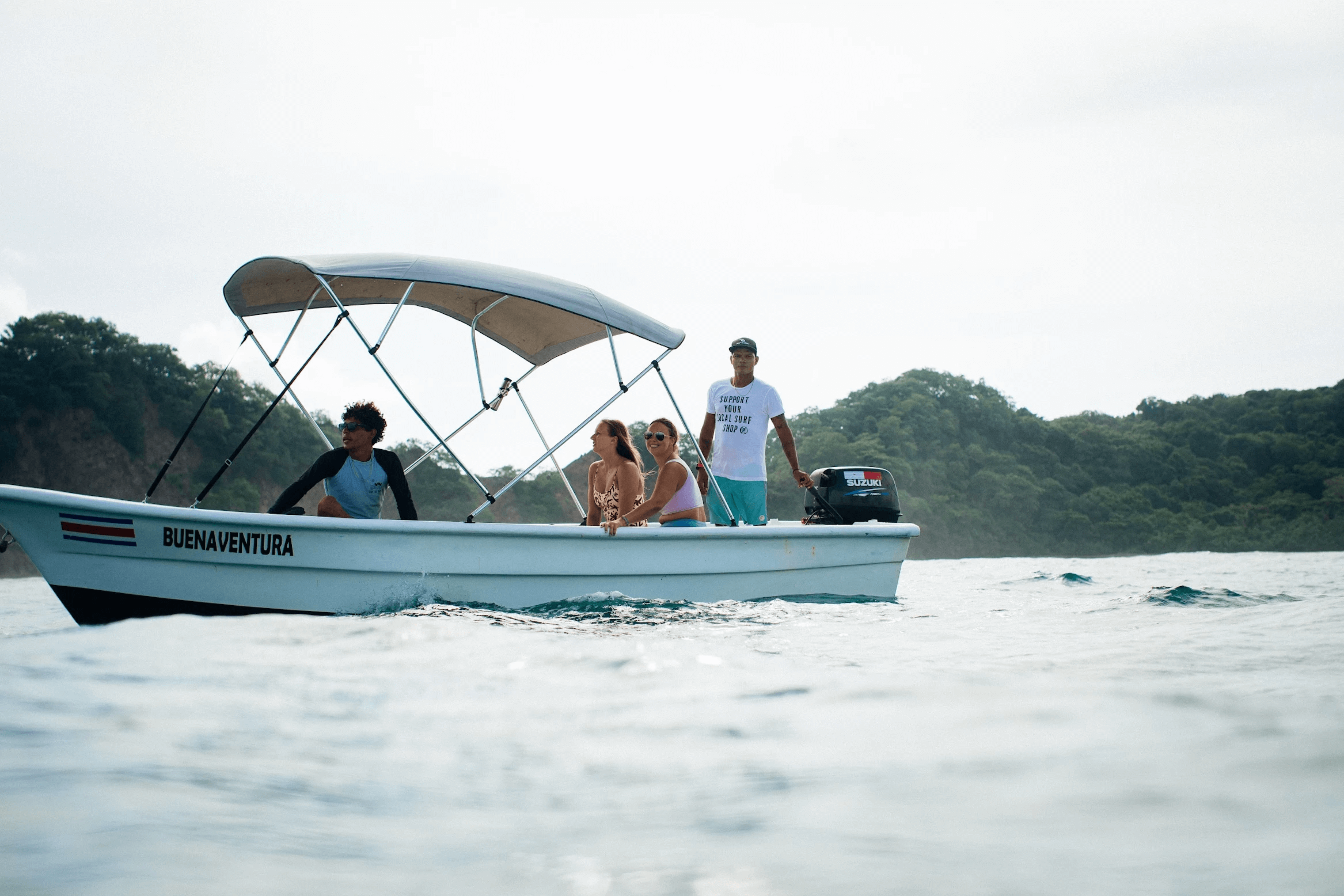 Four people enjoying a boat ride named Buenaventura on calm ocean waters with a forested coastline in the background.