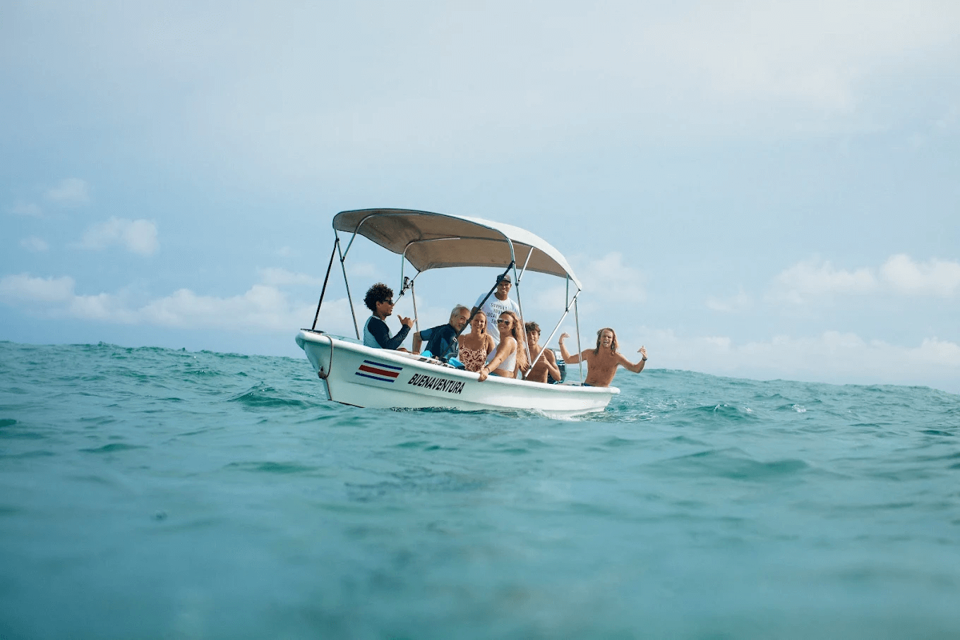 Group of six people on a small white boat named Buenaventura in the ocean under a cloudy sky.