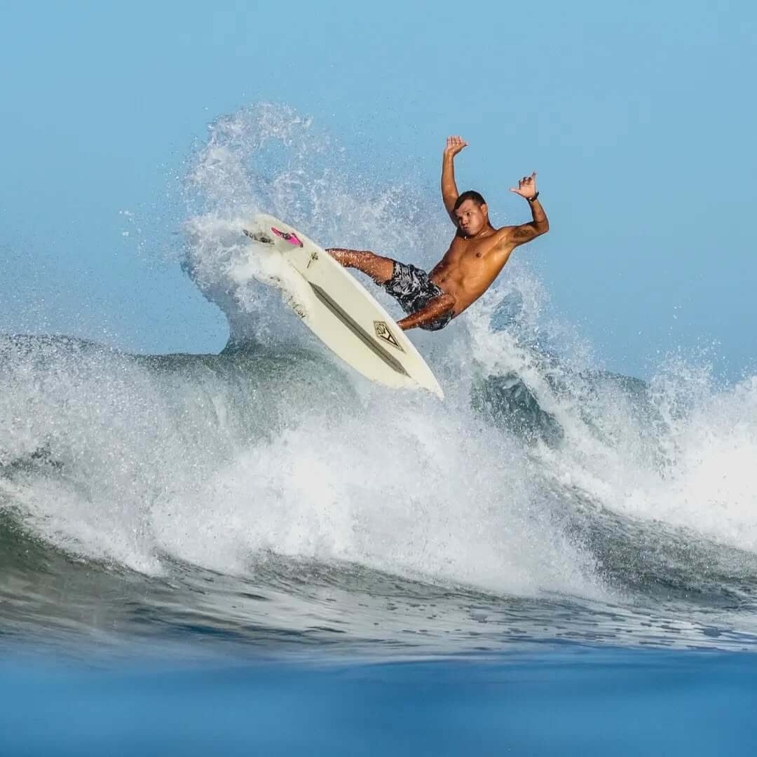 Surfer performing an aerial maneuver above a wave in clear blue water.
