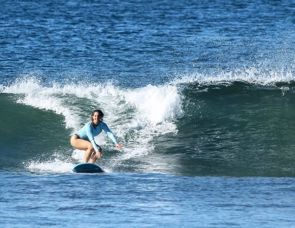 Woman surfing on a blue surfboard riding a breaking ocean wave.